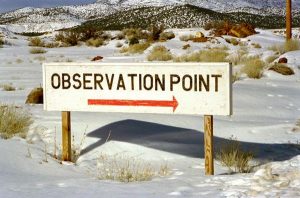 a sign which reads "observation point" with a red arrow against the backdrop of a snowy mountain landscape